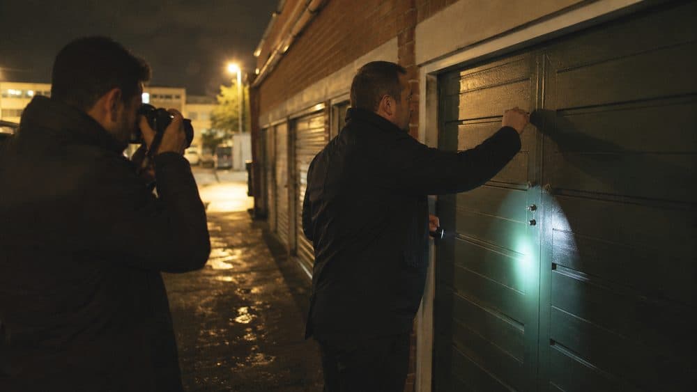 A recovery agent torch in hand at a lock-up garage door at night