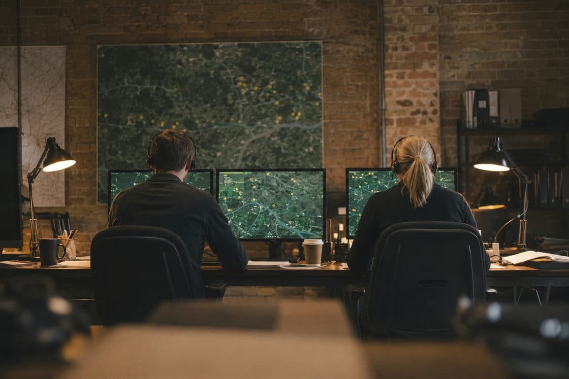 Two analysts on shift at the Bermondsey ops room, map monitors glowing